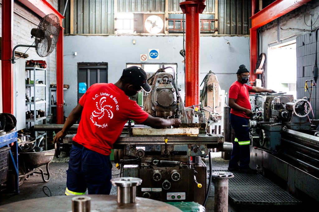 Titan Pumps machine shop: technicians at lathes and milling equipment, red steel structure, L.C. Lister & Son / Titan Pumps SA workwear