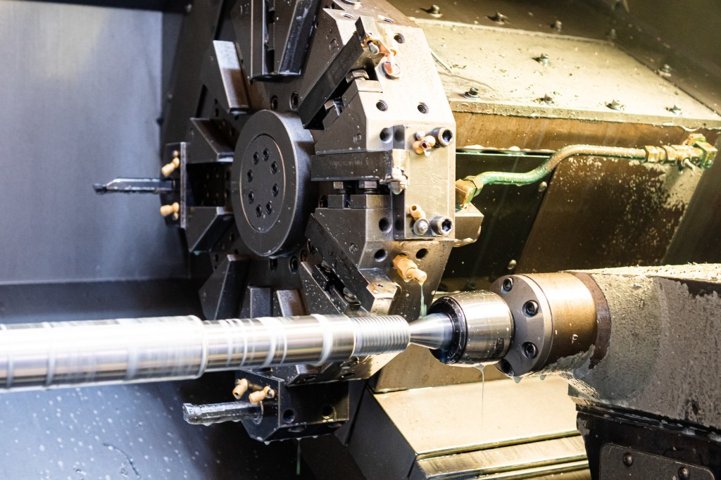 CNC lathe machining a pump shaft: tool turret, coolant spray, precision metal turning in the Titan workshop